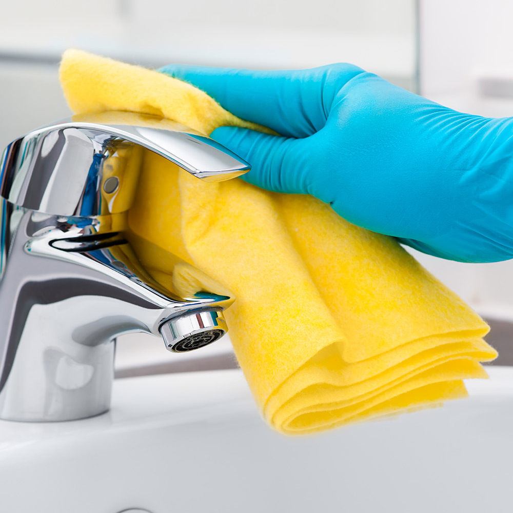 Close up of gloved hand cleaning bathroom sink tap with yellow cloth