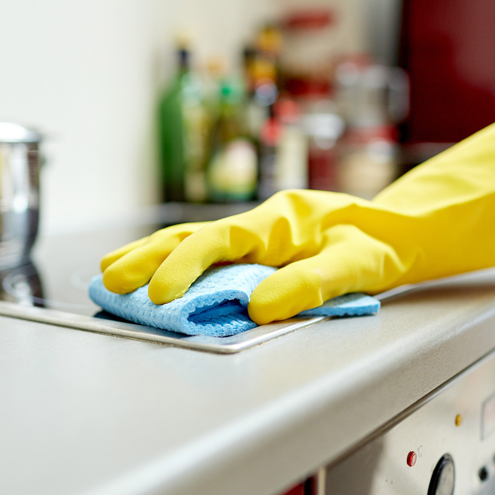 Close up of gloved hand cleaning stovetop with blue cloth